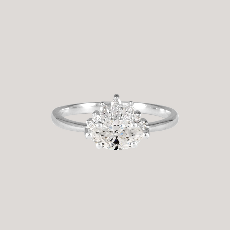 Contemporary take on a traditional marquise diamond ring features an East-West marquise diamond. The centre stone is surrounded with a diamond crown of marquise and round brilliant diamonds. Made in solid 14k or 18K white gold.