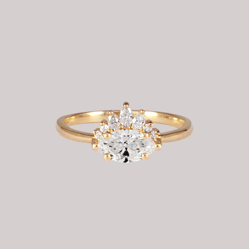 Contemporary take on a traditional marquise diamond ring features an East-West marquise diamond. The centre stone is surrounded with a diamond crown of marquise and round brilliant diamonds. Made in solid 14k or 18K yellow gold.