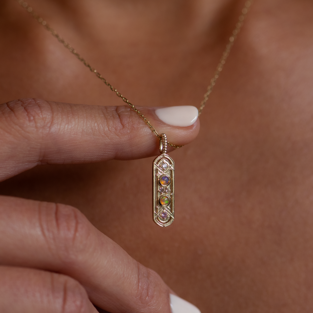 This dainty gold charm, meant to bring balance to your life, featuring two opals and encrusted with the tiniest of diamonds and pink sapphires, made in 14K or 18K gold.
