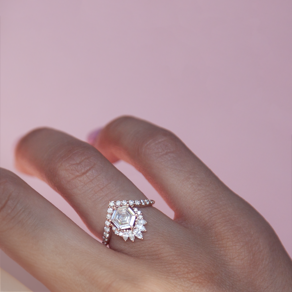 Unique step cut hexagon diamond engagement ring, featuring a delicate V shape band, encrusted with round brilliant diamonds. The hexagon step cut diamond has a low profile setting and is surrounded with a fine crown of marquise and round cut white diamonds. Made in 14k or 18k rose gold.