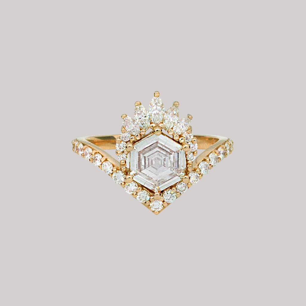 Unique step cut hexagon diamond engagement ring, featuring a delicate V shape band, encrusted with round brilliant diamonds. The hexagon step cut diamond has a low profile setting and is surrounded with a fine crown of marquise and round cut white diamonds. Made in 14k or 18k yellow gold. 