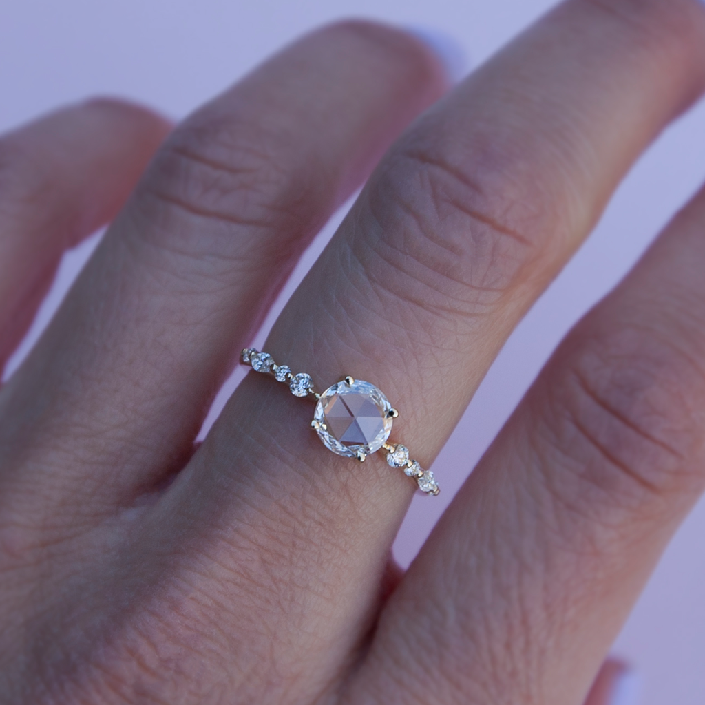 A twist on a classic solitaire engagement ring, featuring a round rose cut diamond, set with four prongs. The main diamond sits on maquise and round brilliant cut diamond band. Made in 14k or 18k yellow gold. 