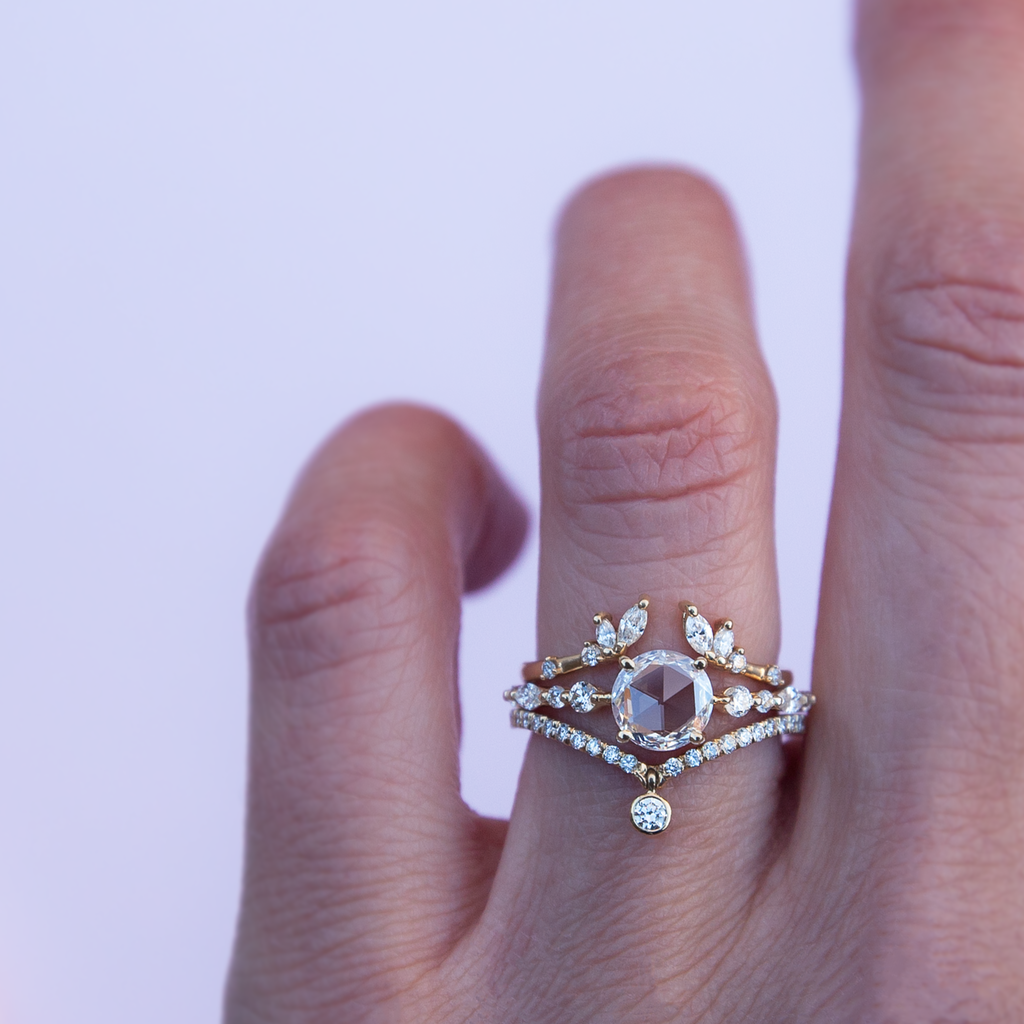 A twist on a classic solitaire engagement ring, featuring a round rose cut diamond, set with four prongs. The main diamond sits on maquise and round brilliant cut diamond band. Made in 14k or 18k yellow gold. 