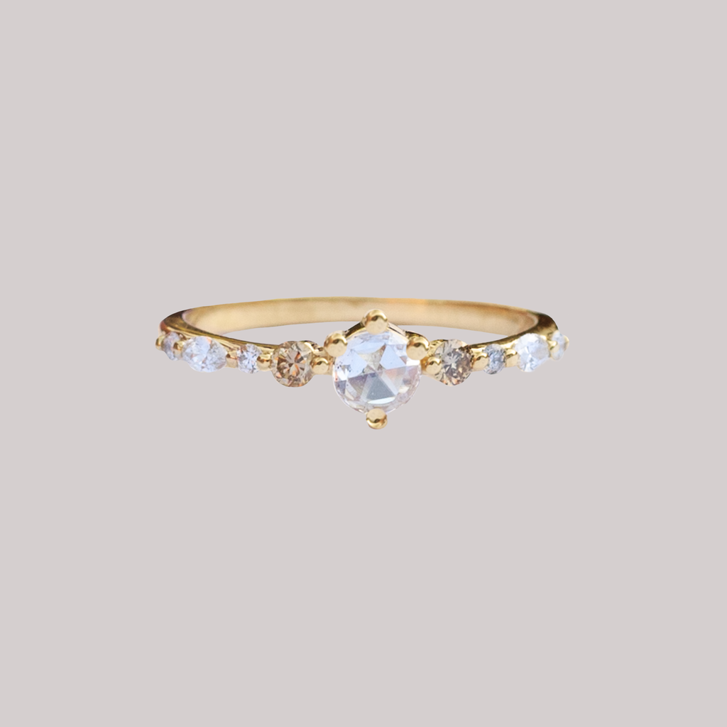 A twist on a classic solitaire engagement ring, featuring a round rose cut diamond, set with four prongs. The main diamond sits on maquise and round brilliant cut diamond band. Made in 14k or 18k gold.