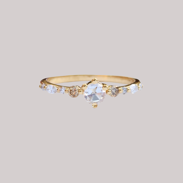 A twist on a classic solitaire engagement ring, featuring a round rose cut diamond, set with four prongs. The main diamond sits on maquise and round brilliant cut diamond band. Made in 14k or 18k gold.