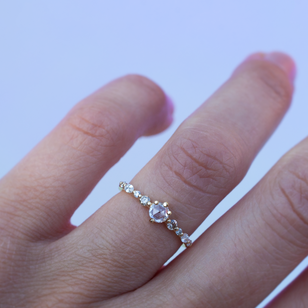 A twist on a classic solitaire engagement ring, featuring a round rose cut diamond, set with four prongs. The main diamond sits on maquise and round brilliant cut diamond band. Made in 14k or 18k yellow gold.