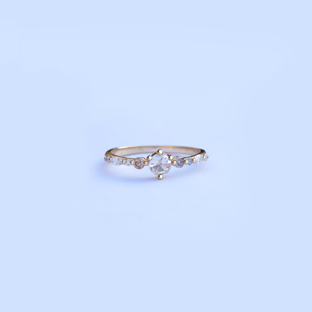 A twist on a classic solitaire engagement ring, featuring a round rose cut diamond, set with four prongs. The main diamond sits on maquise and round brilliant cut diamond band. Made in 14k or 18k yellow gold.